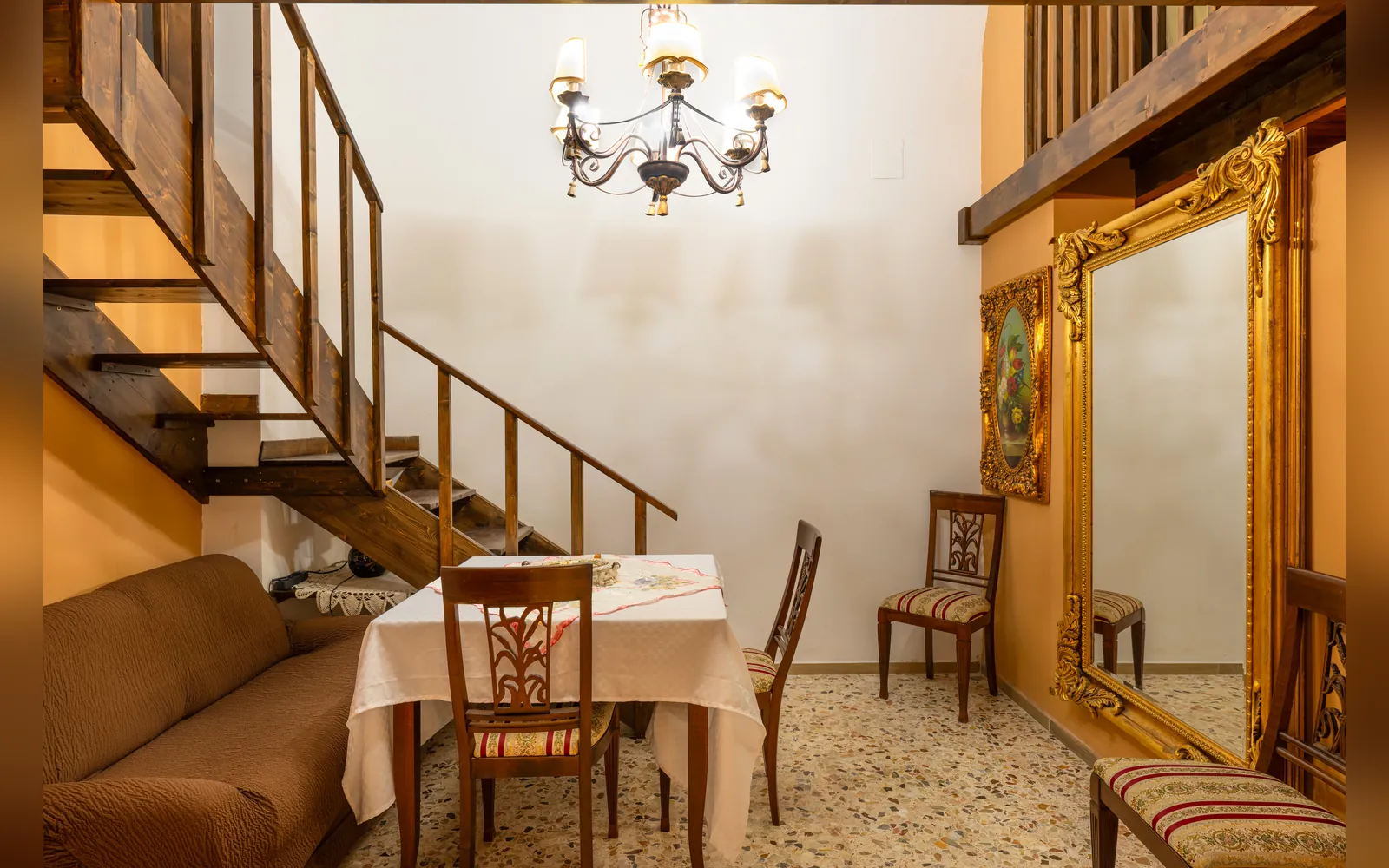 Appartamento MA.GI.A, zona pranzo con divano, specchio dorato e scala in legno