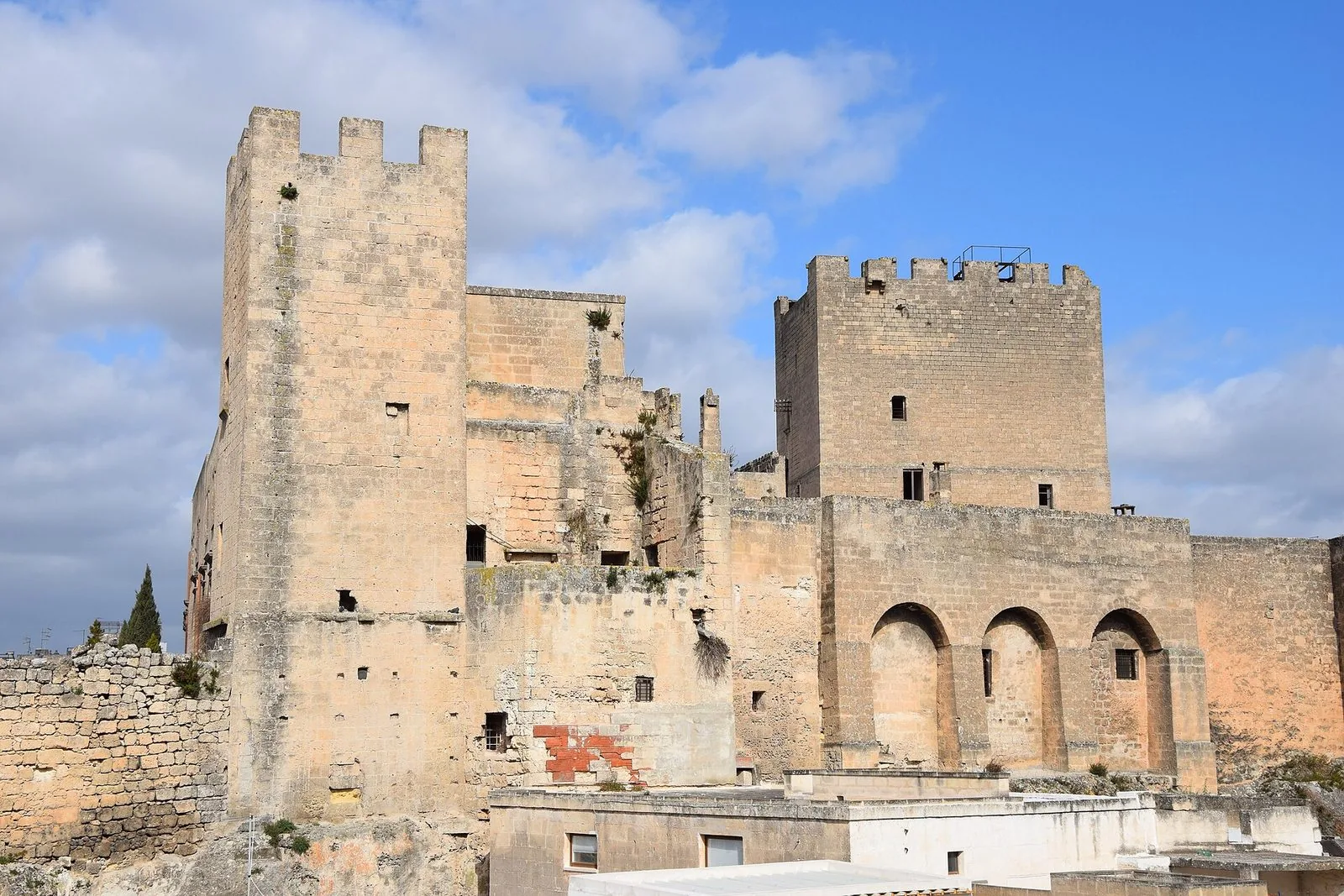 Le torri merlate in pietra chiara del Castello Episcopio di Grottaglie sotto un cielo azzurro con nuvole