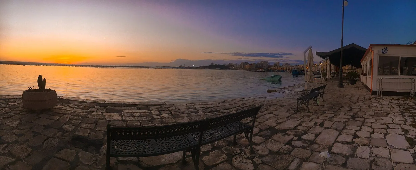 Panorama al tramonto del primo seno del Mar Piccolo visto dalla Città Vecchia di Taranto, con una panchina sul lastricato in primo piano
