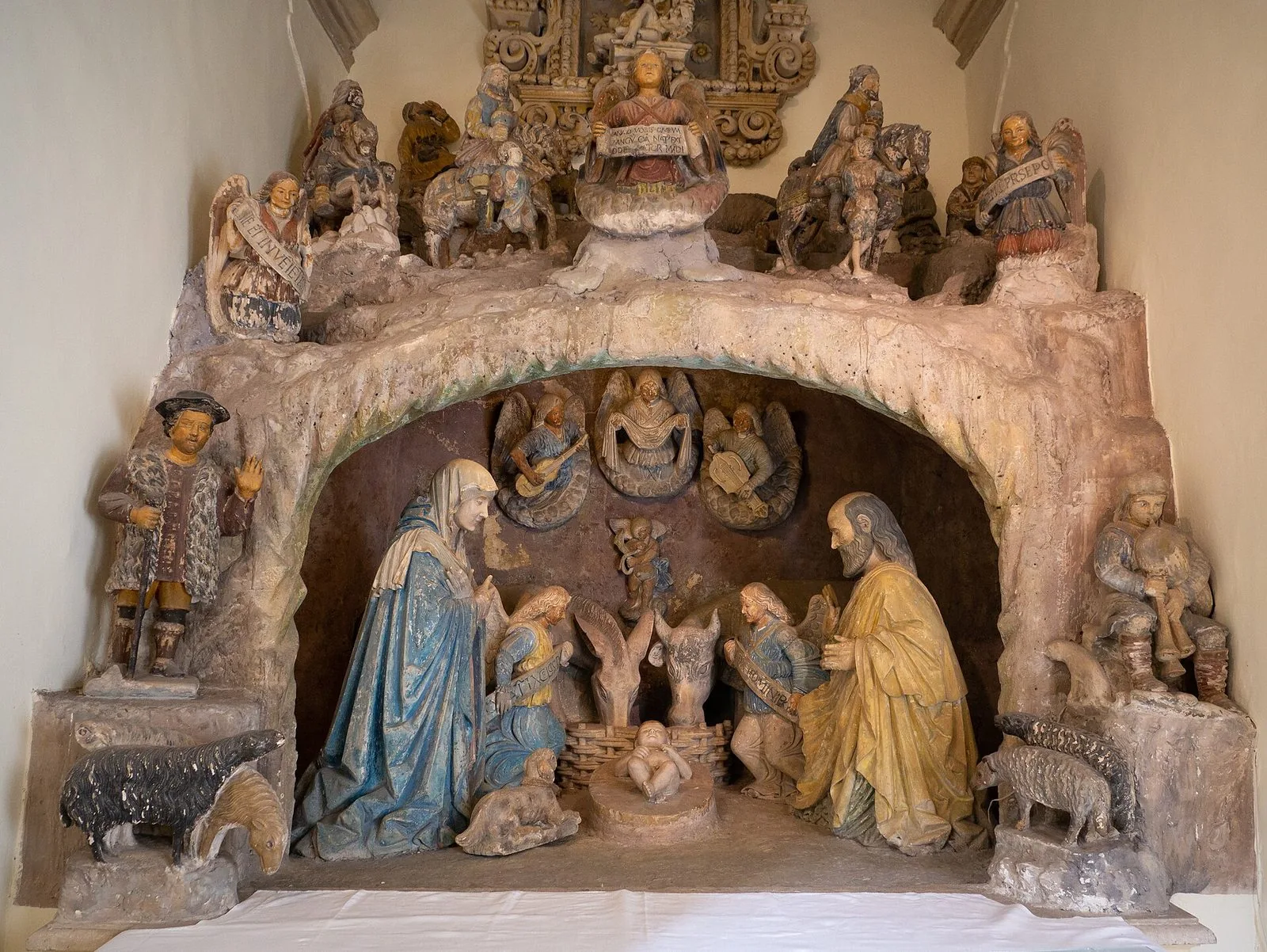 Presepe in pietra policroma di Stefano da Putignano a Grottaglie: la Vergine, San Giuseppe e il Bambino sotto una grotta scolpita, con angeli musicanti, pastori e animali